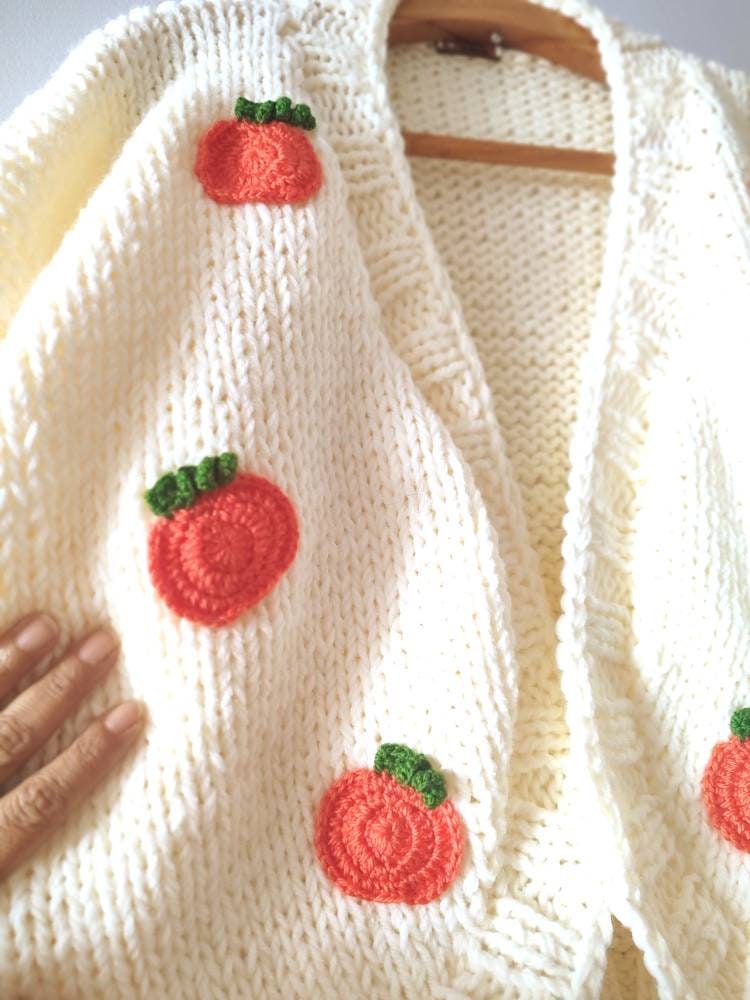 Crocheted orange pumpkins with green leaves sewn onto a cream knit